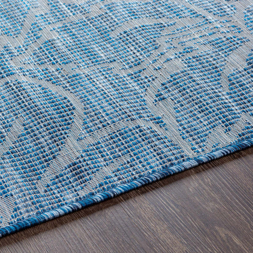 Close-up of the blue and gray woven texture of the Yackandandah Flatweave Area Carpet on a dark wood floor. Texture