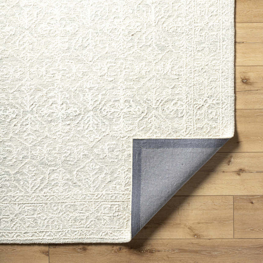 Close-up of a Yadid Sage Wool Area Rug showing its ash and silver gray tones, hand-tufted texture, and backing detail. Fold