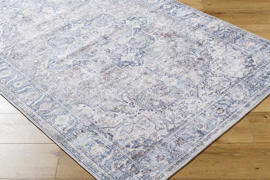 Close-up of the Yoshi Washable Area Rug in denim, cream, and gray with a traditional, distressed pattern on wood floor. Corner