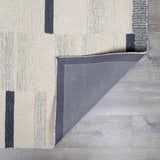 Close-up of the Aibonito hand-tufted wool area rug featuring a beige and charcoal geometric design and gray backing. Fold