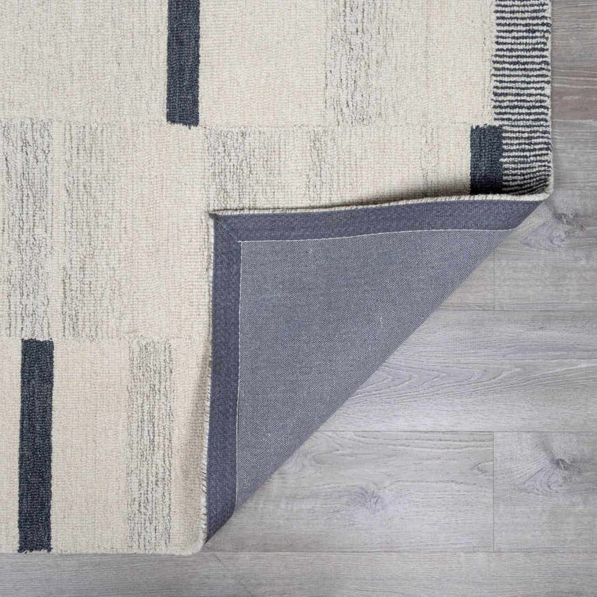 Close-up of the Aibonito hand-tufted wool area rug featuring a beige and charcoal geometric design and gray backing. Fold