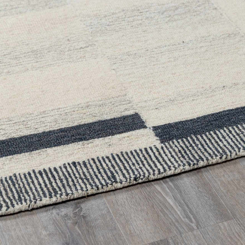 Close-up of the Aibonito rug. Hand-tufted wool rug in beige and charcoal with a geometric pattern and striped border. Corner