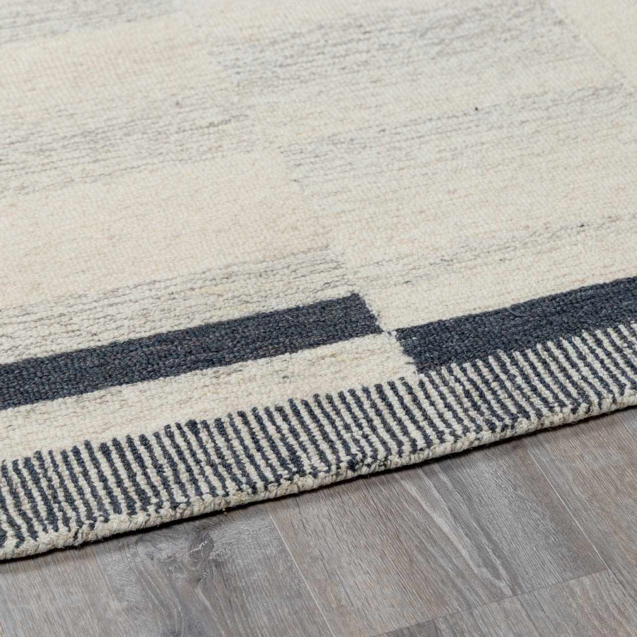 Close-up of the Aibonito rug. Hand-tufted wool rug in beige and charcoal with a geometric pattern and striped border. Corner