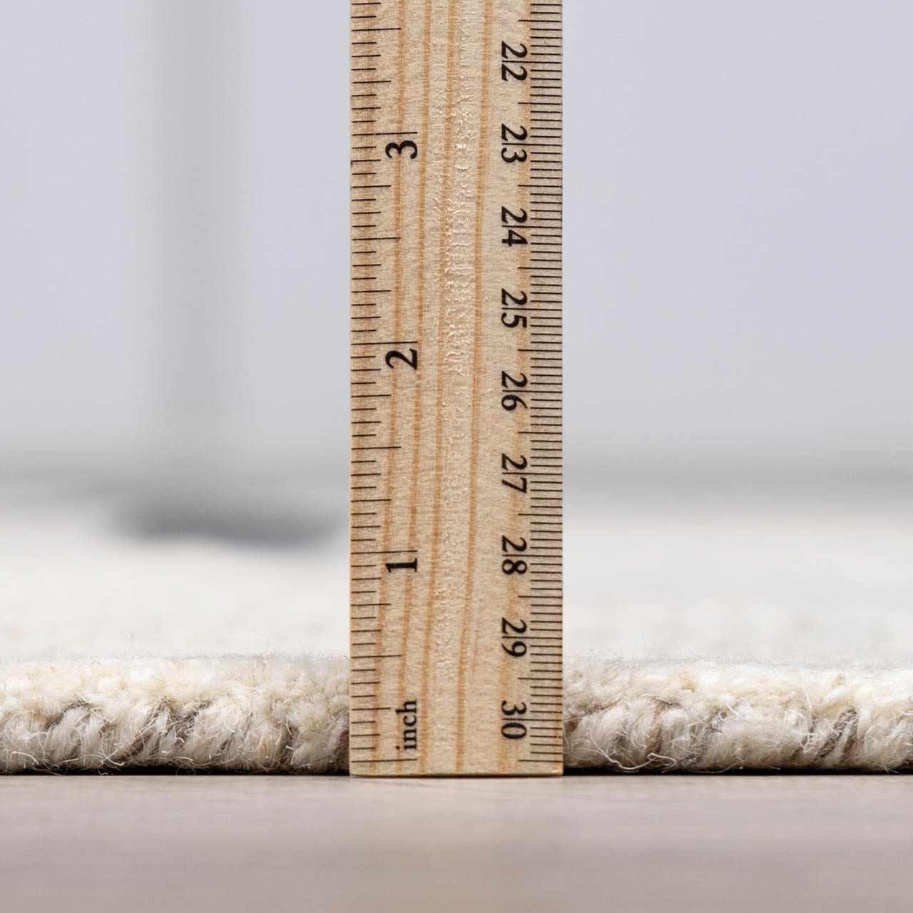 Close-up of the Aibonito Hand Tufted Wool Area Rug showing its thickness with a ruler. Beige wool rug. Pile