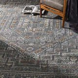 Living room scene with charcoal Akle Premium hand-knotted wool area rug, gray chair, and open book. Contemporary style. Styleshot