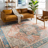 Living room scene with a Livabliss Amelie AML-2309 rug, tan sofa, wood chair, and bookshelf. The rug has beige, rust, and blue tones. Roomscene-Rectangle