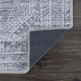 Close-up of the Barny Gray Blue Washable Rug showing its traditional pattern, charcoal and off-white colors, and non-slip backing. Fold