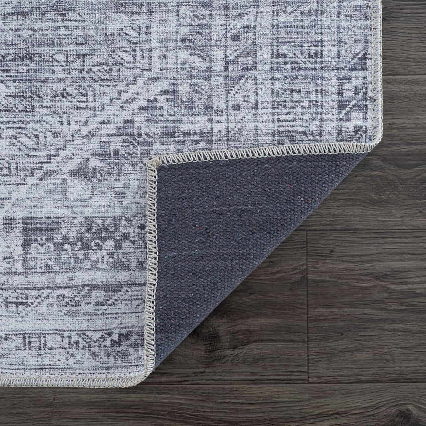 Close-up of the Barny Gray Blue Washable Rug showing its traditional pattern, charcoal and off-white colors, and non-slip backing. Fold