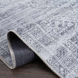 Close up of the Barny Gray Blue Washable Rug showing its chenille texture, gray and off-white colors, and woven backing. Fold