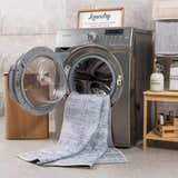 Barny Gray Blue Washable Rug in a bright laundry room with gray tile, next to a washing machine and wooden shelf. Washing-Machine
