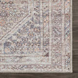 Close-up of the Barny Tan Washable Area Rug, showcasing its traditional design, tan, gray, and peach hues, and woven texture. Corner