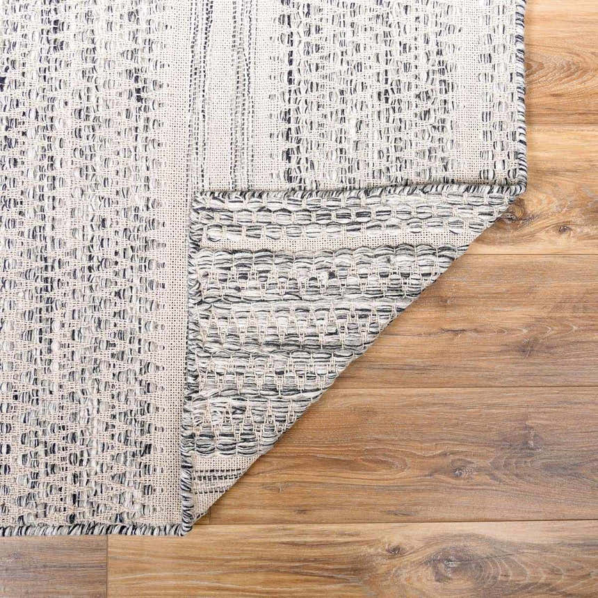 Close-up of the hand-woven Arabi Wool Area Rug. Black, gray, and light beige wool rug with a textured, farmhouse design. Fold