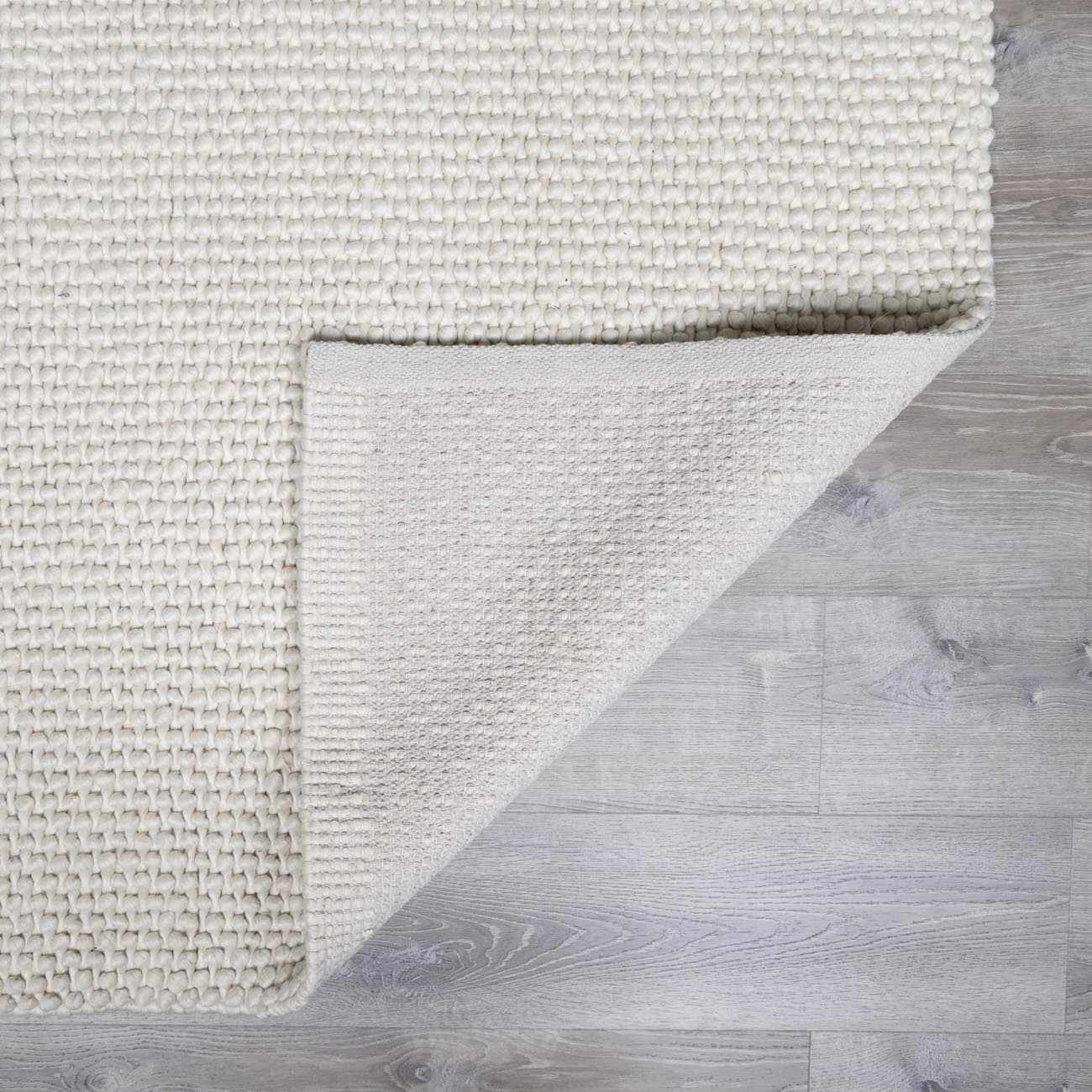 Close-up of the textured, hand-woven Lucerne Plain Cream Wool Rug LNE-1000 showing the backing. Fold