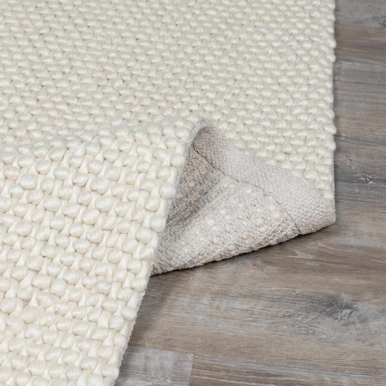 Close-up of the textured weave of the Lucerne Plain Cream Wool Rug, showing its looped pile and backing. Fold