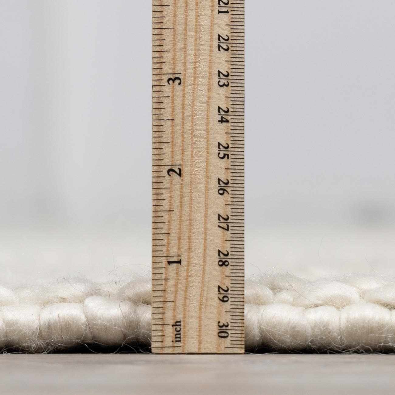 Close-up of the Lucerne Plain Cream Wool Rug texture with a ruler to show pile height. Pile