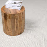 Close-up of the cream Lucerne Plain Wool Rug, with a textured weave and a rustic wood side table. Styleshot