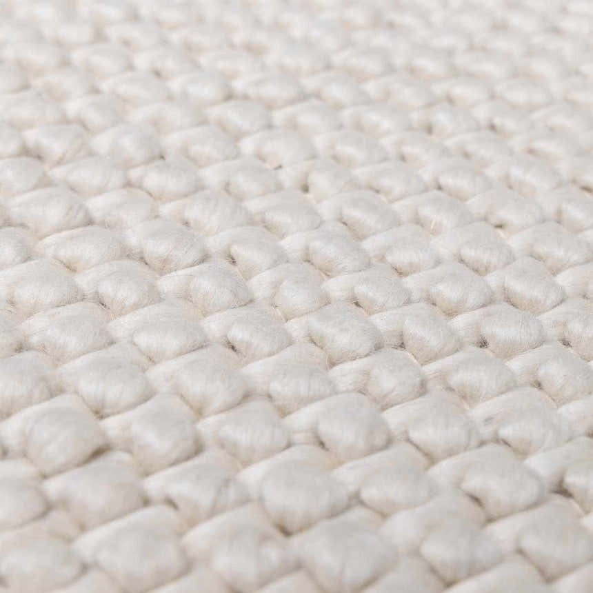 Close-up of the hand-woven texture of the Lucerne Plain Cream Wool Rug. Cream-colored wool rug with a basket weave pattern. Texture