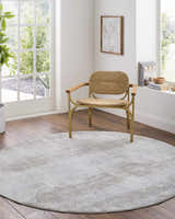 Light-filled room with a round Avani Thick Luxe Boutique Rug in gray tones under a woven chair. Roomscene-Round