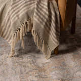 Close-up of the Vaeda Blue & Beige Thick Luxe Rug with beige, tan, and blue tones under a chair with a fringed throw. Styleshot