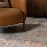 Close up of the beige, blue, and pink floral pattern of the Vaeda Blue & Beige rug under a tan leather chair. Styleshot
