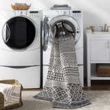 Laundry room scene with Barnwood Washable Area Rug emerging from the washing machine. Bohemian black and cream geometric pattern. Washing-Machine