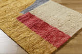 Close-up of the hand-tufted Budrys Wool Area Rug. Brick red, camel, pearl and gray blocks on a tan, textured rug. Corner