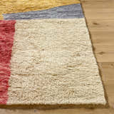 Close-up of a hand-tufted Budrys Wool Area Rug. Features brick red, camel, and pearl colors, with a contemporary design. Front