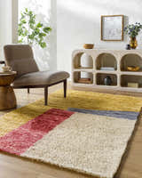 Living room scene with a Budrys Wool Area Rug in brick red, camel, tan and pearl, styled with a modern chair and light wood console table. Roomscene-Rectangle
