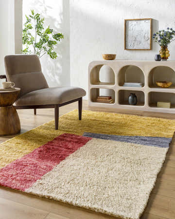 Living room scene with a Budrys Wool Area Rug in brick red, camel, tan and pearl, styled with a modern chair and light wood console table. Roomscene-Rectangle