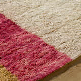 Close-up of the hand-tufted Budrys Wool Area Rug. Features a brick red, camel, and light wood color palette. Texture