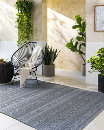 Sunlit patio scene with gray Brayan Area Rug, modern chair, and lush greenery creating a relaxing, transitional space. Roomscene-Rectangle
