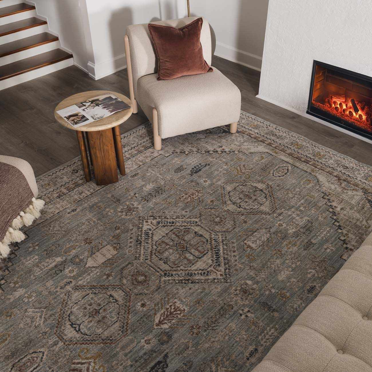 Living room scene with a Kouta Gray Blue area rug, beige chair, fireplace, and wood accents for a cozy, traditional feel. Roomscene-Rectangle