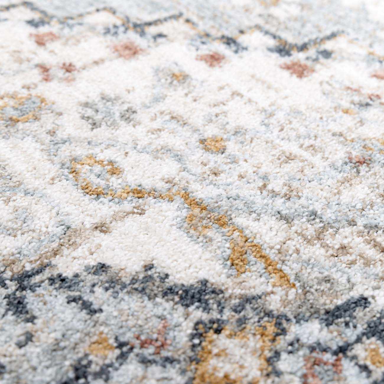 Close-up of the Kouta Gray Blue Area Rug. Features a traditional pattern in off-white, gray, blue, and mustard hues. Soft, textured weave. Texture