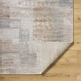 Close-up of the Anaisa Beige Luxe Thick Area Rug showing geometric patterns and neutral colors on a wood floor. Fold