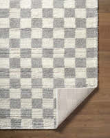 Close-up of Belita Tan Luxe Shag Area Rug with cream and light gray checkerboard pattern on a wood floor. Fold