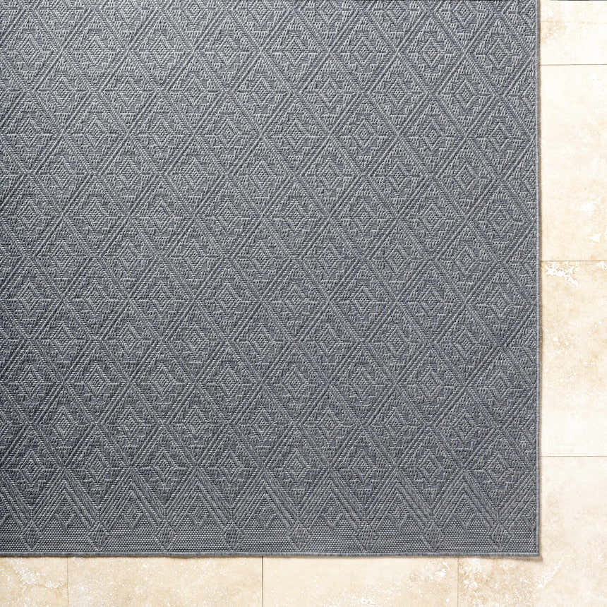 Close-up of the Bandit Gray Area Rug showing its diamond pattern and woven texture on a beige tile floor. Corner