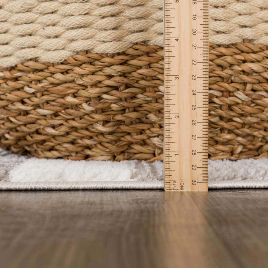 Close-up of the Bojana Broken-Striped Area Rug showing pile height with a ruler and decorative basket. Cream and off-white tones. Pile