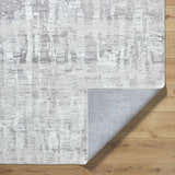 Close-up of the Branka Area Rug showing its light silver and gray contemporary pattern and texture on wood floor. Fold
