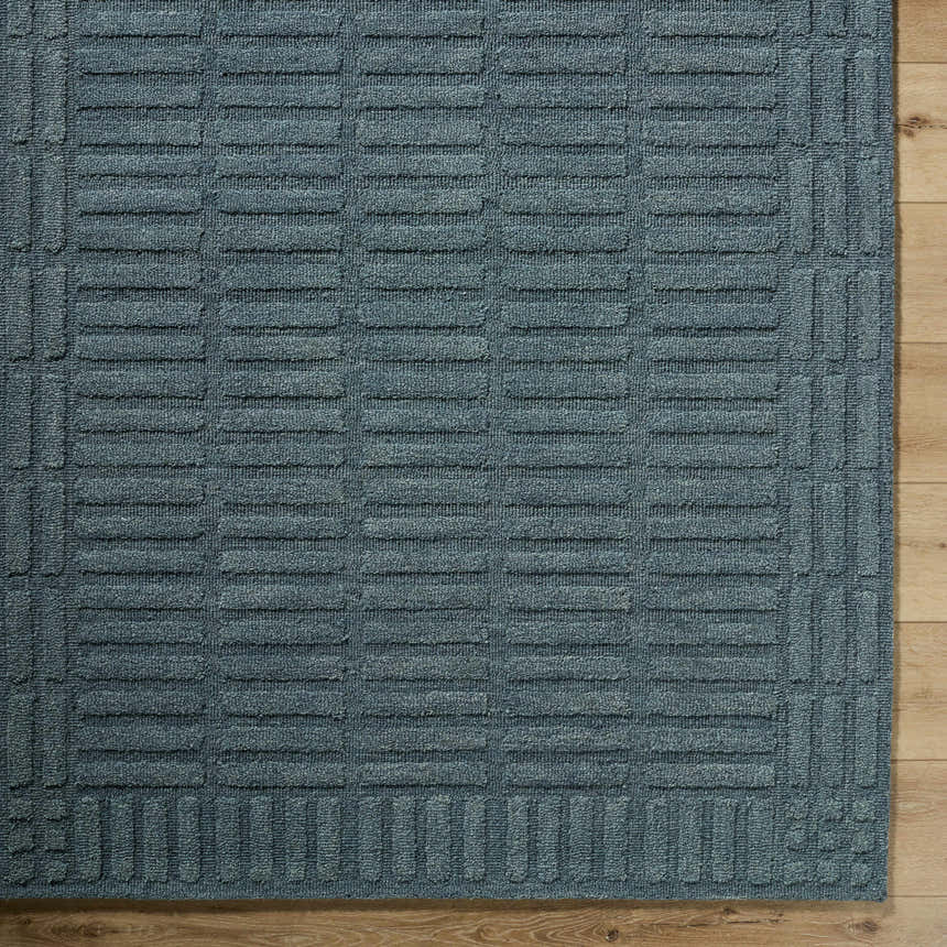 Close-up of the hand-tufted Birger Slate Blue Area Rug. The 100% wool rug features a contemporary geometric pattern. Corner