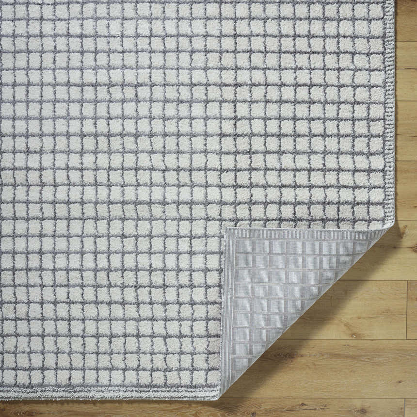 Close-up of the Balint Area Rug. Charcoal and light gray squares pattern. Machine woven texture. Fold