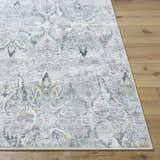 Close-up of the Bryony Area Rug. Traditional farmhouse design in light silver, silver gray, and slate blue on wood floor. Front