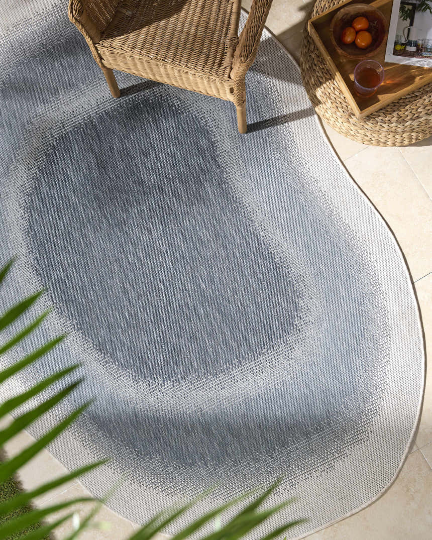 Outdoor patio scene with a blue and cream Burian Blue Area Rug, wicker chair, and side table. Roomscene-Custom