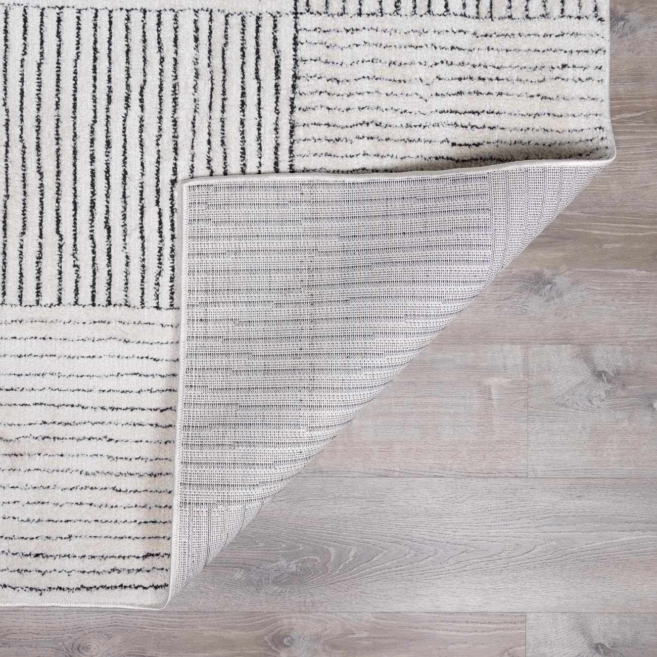 Close-up of the Modern Scandi Architect I Area Rug. Ivory rug with black stripes and geometric pattern. Machine woven polyester. Fold