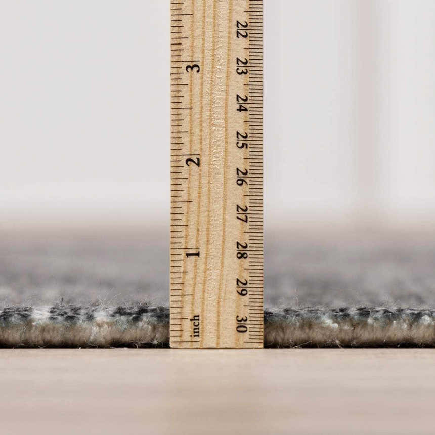 Close-up of the Janek II Modern Abstract Area Rug showing its pile height with a ruler. Neutral colors and soft texture. Pile