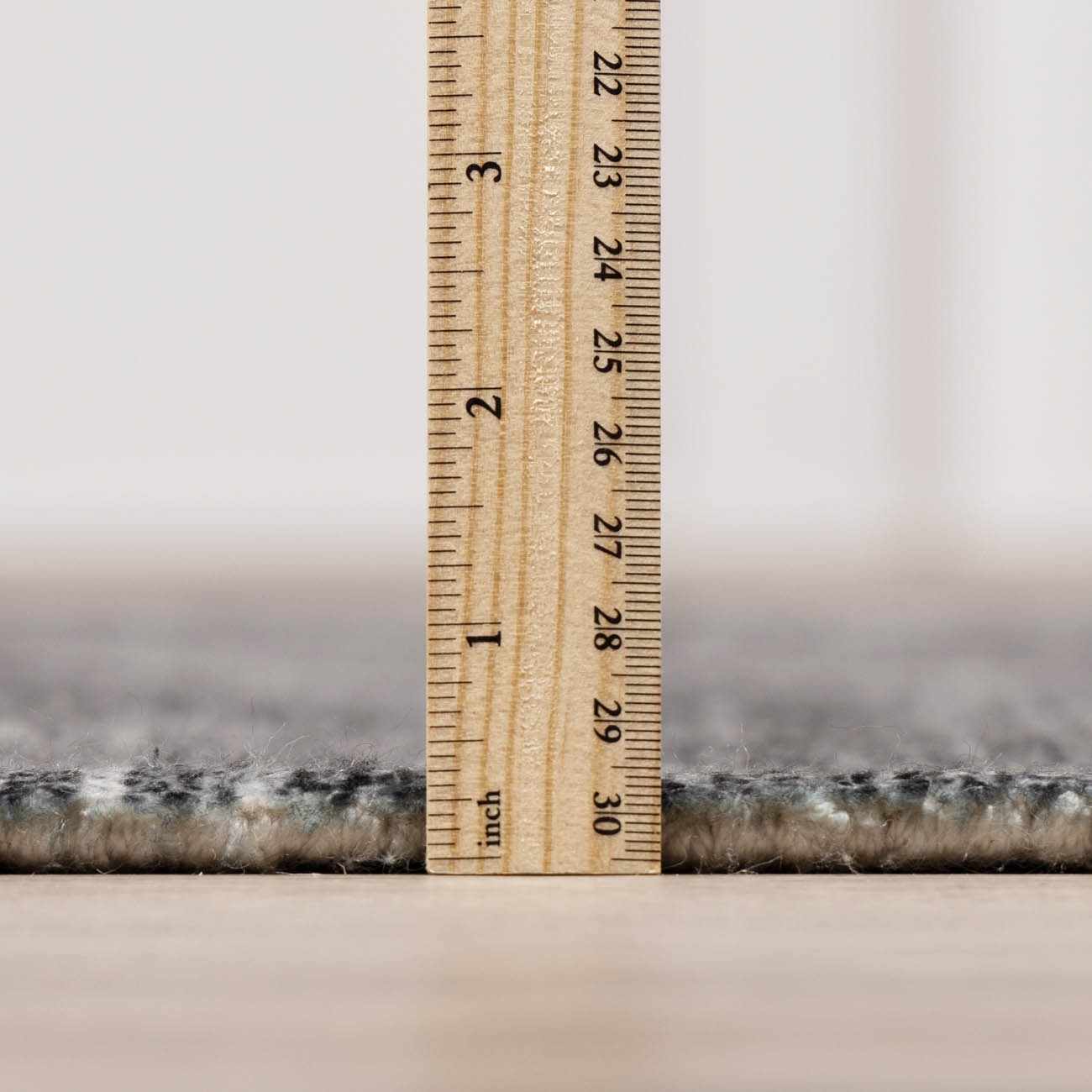 Close-up of the Janek II Modern Abstract Area Rug showing its pile height with a ruler. Neutral colors and soft texture. Pile