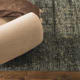 Close-up of the Janek II Modern Abstract Area Rug in gray and beige, with a textured pattern and a neutral-toned sofa. Styleshot