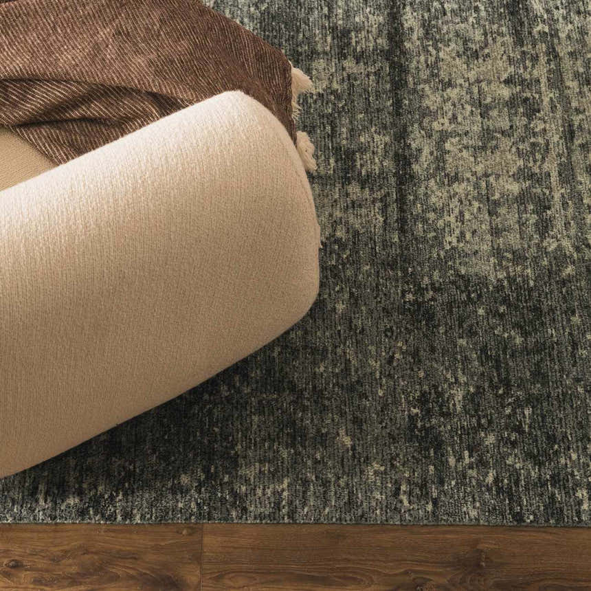 Close-up of the Janek II Modern Abstract Area Rug in gray and beige, with a textured pattern and a neutral-toned sofa. Styleshot