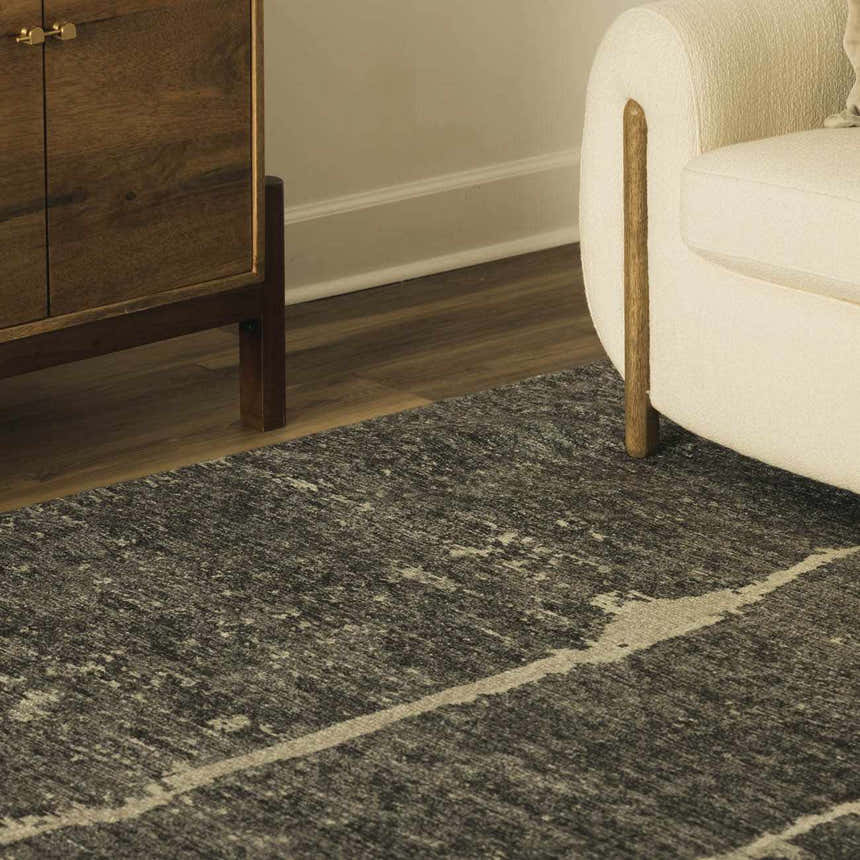 Close-up of a Janek II Modern Abstract Area Rug in a living room with a wood cabinet and cream armchair. Roomscene-Rectangle