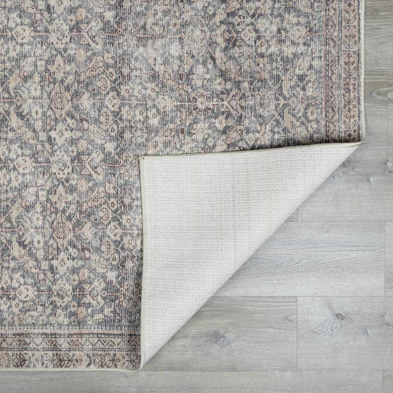 Close up of the beige, red, and green Collins Avenue III Vintage Damask Area Rug showing the rug's backing. Fold