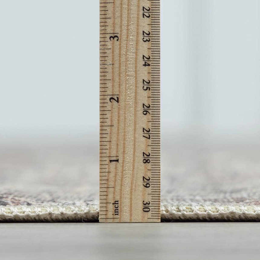 Close-up of the Collins Avenue III Vintage Damask Area Rug showing its pile height with a ruler. Beige, red, green, and ivory colors. Pile